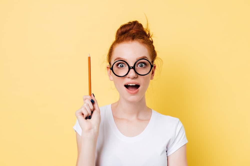 Girl wearing glasses holding a pencil upright.