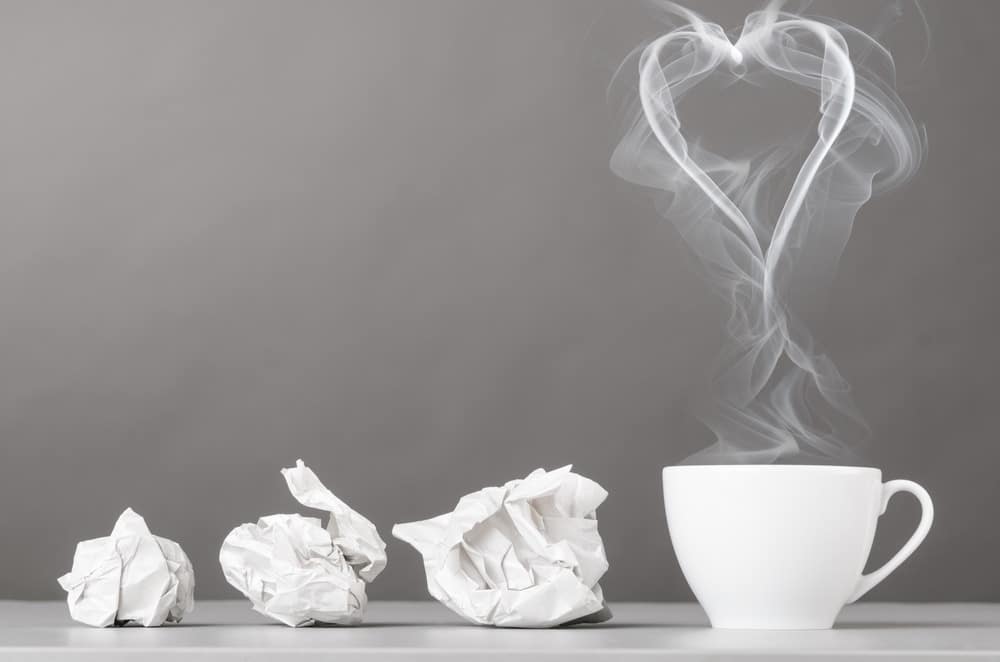 3 pieces of scrunched up paper next to a white coffee mug, with a love heart on top