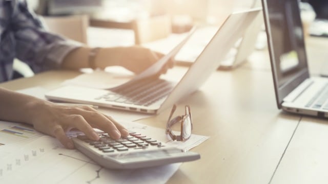 A person using a calculator with some laptops around