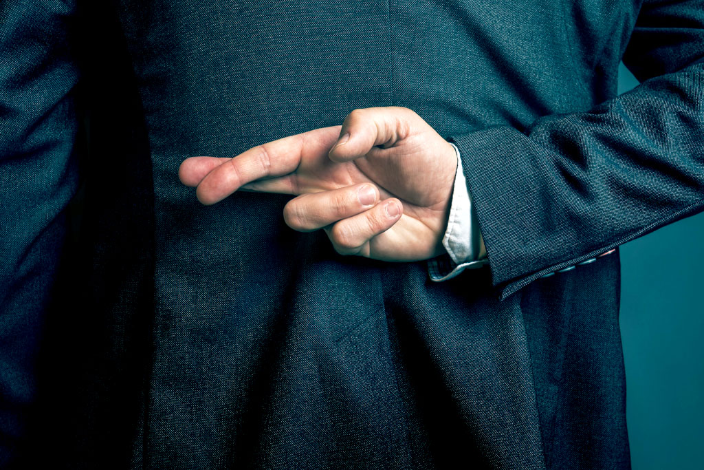 Man fingers crossed behind him wearing a black suit