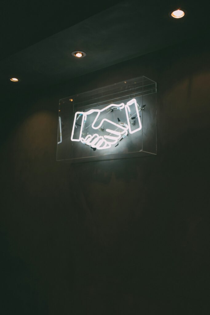 a neon sign with handshake on a wall